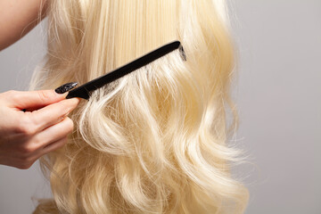 Hairdresser combing blonde hair with black plastic comb closeup
