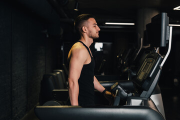 Fototapeta na wymiar guy athlete runs on a treadmill in the gym. dark background