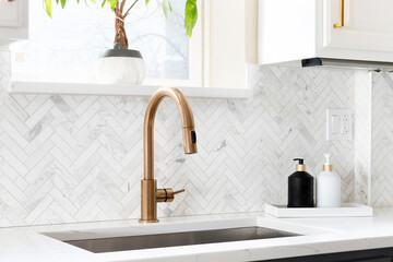 Sink detail shot in a luxury kitchen with herringbone backsplash tiles. white marble countertop,...