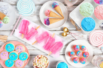 Pastel summer sweets table scene. Assortment of ice cream, popsicles, cookies and treats. Above...