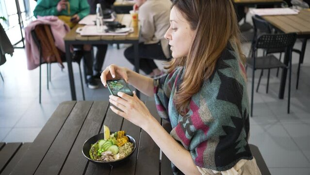 Young woman makes photo of food with mobile phone camera in cafe. Woman takes pictures of tasty dish for social network. Guest takes photo of lunch bowl