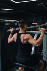 guy athlete shakes his back on the simulator in the gym. dark background