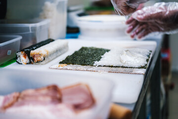 sushi maker prepares rolls puts rice on a sheet of nori