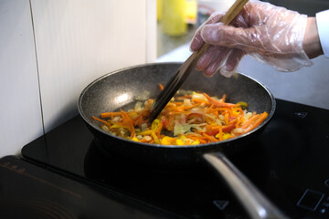 cooks chopped vegetables in a frying pan stirring with a spatula