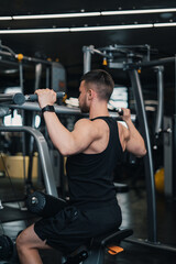 Obraz na płótnie Canvas guy athlete shakes his back on the simulator in the gym. dark background