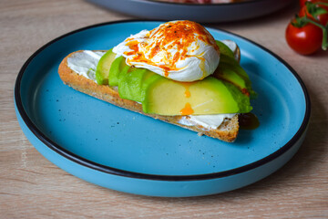 Poached Benedict Egg on a slice of baguette with avocado and cherry tomatoes.