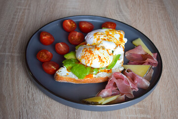 Poached Benedict Egg on a slice of baguette with avocado and cherry tomatoes.