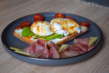 Poached Benedict Egg on a slice of baguette with avocado and cherry tomatoes.