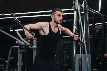 Fototapeta na wymiar the guy pumps his chest on the simulator in the gym. dark background