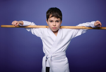 Confident strong European aikido wrestler posing with wooden aikido weapon against violet background with copy ad space. Oriental martial arts practice