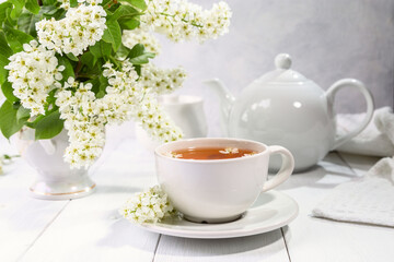 Useful spring tea with bird cherry in a white cup on a light background