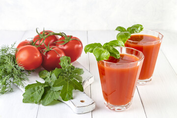 Tomato juice with basil and tomatoes on a light wooden background