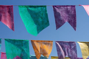 Várias bandeirolas coloridas penduradas com céu azul ao fundo.