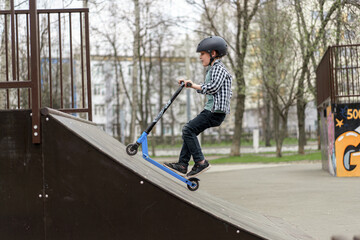 A boy on a scooter and in protective helmet do incredible stunts in skate park. Extreme jump. The concept of a healthy lifestyle and sports leisure © alenaphoto