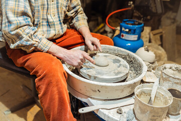 male hands of master potter are sculpting clay pottery sitting at potter's wheel. authentic atmosphere, artist's creative workshop