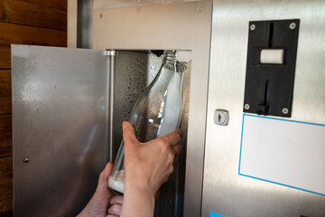 Automatic kiosk selling raw milk from the farm. Hand holds a bottle into which a fresh dairy...
