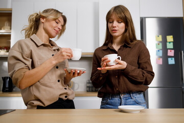 Mom and daughter drink coffee and cosy chat in the kitchen