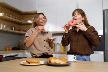 Mom treats her daughter with tasty donuts during a tea time in the kitchen