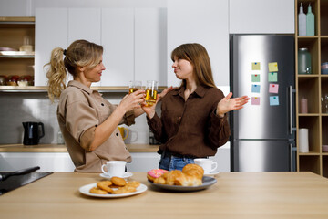 Daughter and mother drinking juice and talking about personal things in the kitchen
