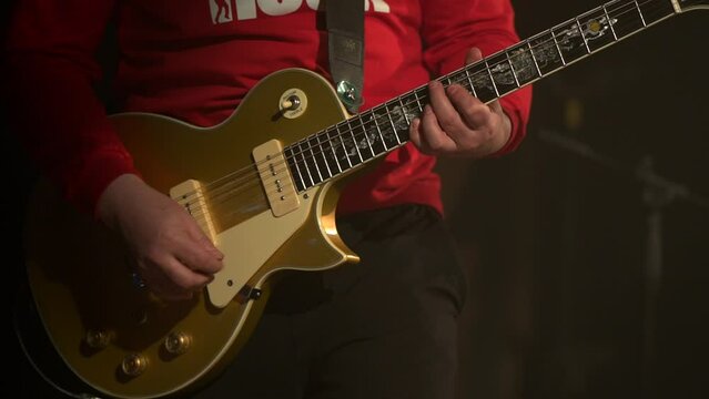 The guy in the red T-shirt plays the golden guitar. Rhythm guitarist on stage in a club. Live performance of a rock band