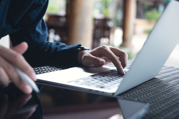 Business man working on laptop computer and using digital tablet, surfing the internet at coffee shop, close up. Man freelancer online working from cafe
