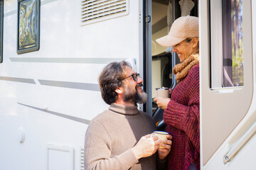 Mature couple enjoy leisure activity outside a camper van with coffee mug. Travel people smile...
