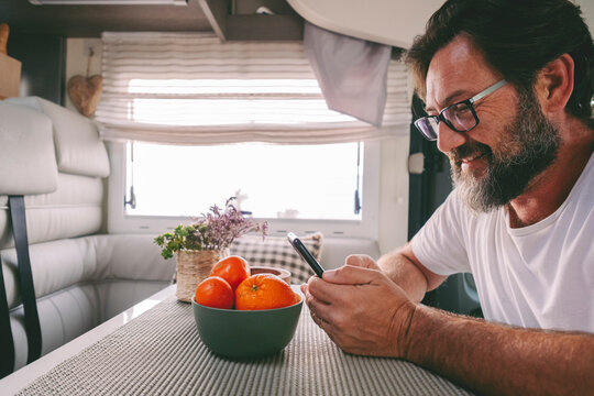 Side portrait of mature handsome man using phone sitting on a camper van. People and travel lifestyle with everywhere connection. People communicate during travel road trip. Planning destination