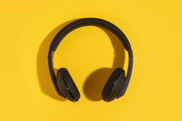 Fototapeta na wymiar Wireless black headphones on a yellow background. Top view.