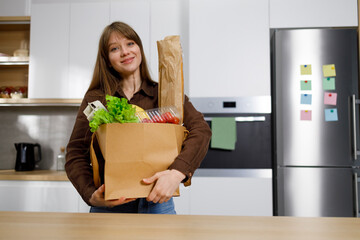 Portrait of beautiful young woman with grocery in paper shopping bag at home kitchen