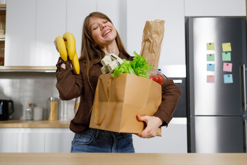 Joyful young housewife with a full package of groceries after shopping stands in the kitchen