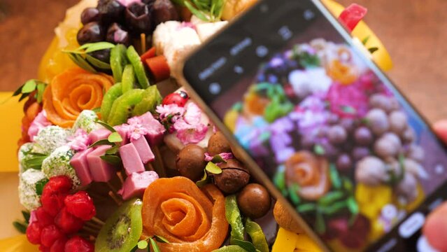 a tasty gift handmade cake bouquet of healthy dried fruits nuts takes pictures on a smartphone camera.Selective focus.A confectioner takes pictures of his created delicious culinary masterpiece
