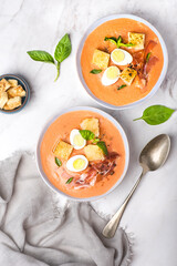 Spanish salmorejo soup, tradition Andalusian cold tomato soup topped with serrano ham (jamon), boiled egg, bread and pepper on the white background. Summer cold recipes