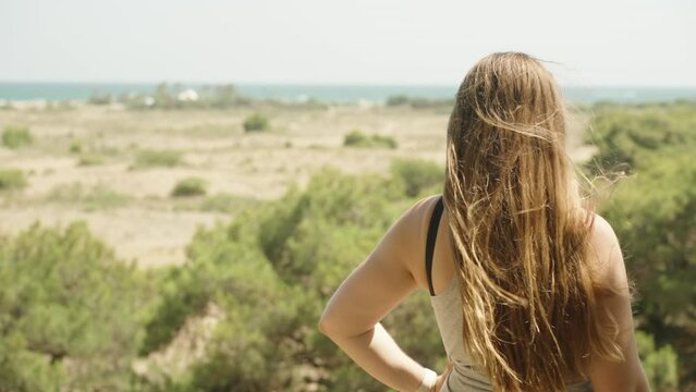Long hair blows in the wind. Girl is looking at the sea in the distance. Slow mo