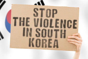 The phrase " Stop the violence in South Korea " is on a banner in men's hands with a blurred South Korean flag in the background. Sad. Rights. Security. Social. Stress. Combat. Hate. Cruelty