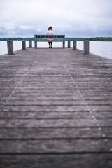 Una chica sentada en el extremo de un embarcadero de madera frente a un lago.