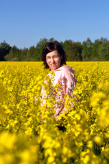 Naklejka na ściany i meble Beautiful young woman in the middle of a field of yellow rapeseed or canola flowers.