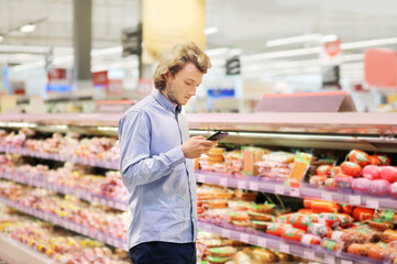 Young man shopping in supermarket, reading product information.