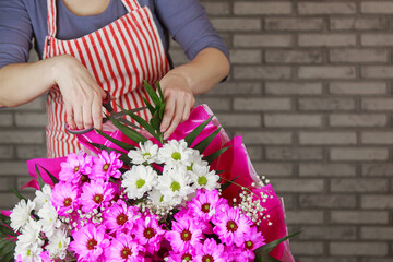 a female florist ties a ribbon bow on a bouquet of flowers wrapped in craft paper on the desktop. Top view.