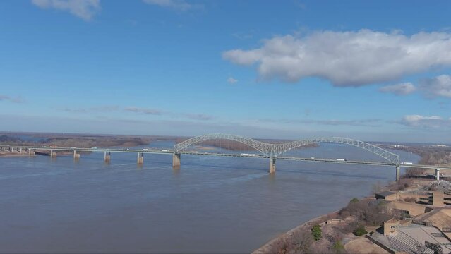aerial footage of the Hernando de Soto Bridge over the vast flowing waters of the Mississippi river with cars and trucks driving across the bridge and blue sky with clouds in Memphis Tennessee USA