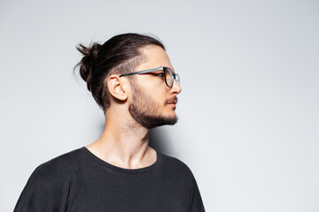 Side portrait of young guy with hair bun wearing eyeglasses on grey background.