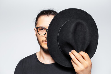 Close-up portrait of young man hides half face with black hat on white.