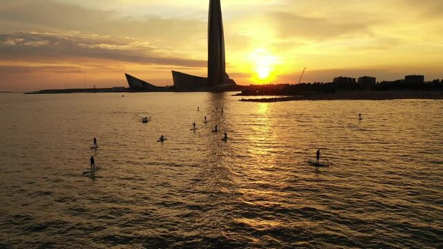Aerial view of a group of girls and boys in the Gulf of Finland at sunset, rowing on a Sup board. The first lesson with the instructor. Russia, St. Petersburg, 05.06.2021