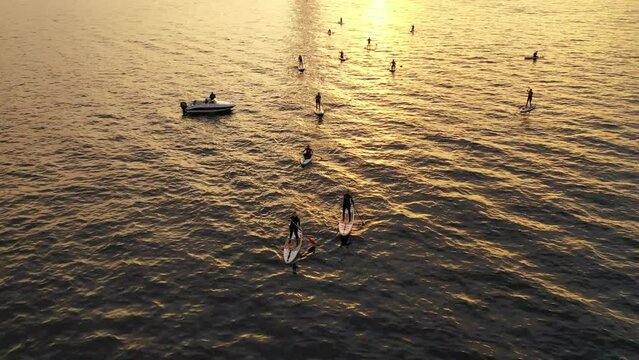 Aerial view of a group of girls and boys in the Gulf of Finland at sunset, rowing on a Sup board. The first lesson with the instructor. Russia, St. Petersburg, 05.06.2021