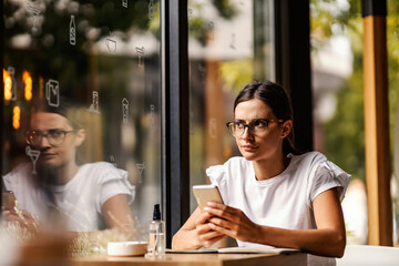 An angry college girl is sitting in a coffee shop and writing messages to someone.