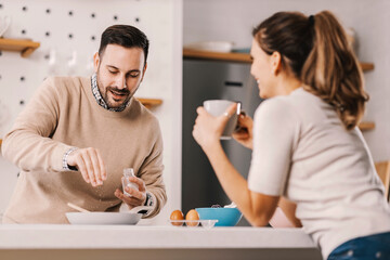 A man adding salt in breakfast while standing in kitchen with girlfriend.