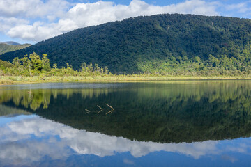 Stunning reflection of bush-clad mountains in calm surface of Lake Moeraki