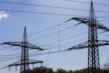 Electrical net of poles on a panorama of blue sky and green meadow.