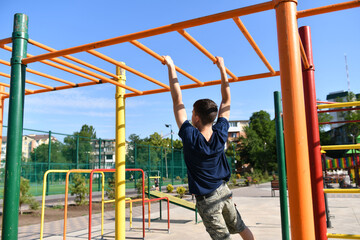 a teenage boy trains on a sports ground outdoors, he does physical exercises, a healthy lifestyle, a bright sunny day in summer