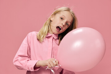  joyful school-age girl stands on a pink background with a big balloon in her hand and smiles broadly while looking at the camera. Horizontal photo with blank space for advertising layout insert