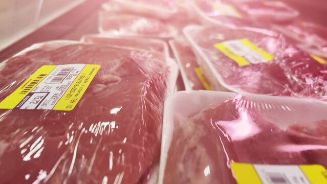 Raw chicken and turkey fillets in cling-wrapped plastic containers are on display in a supermarket refrigerator. Close-up shot